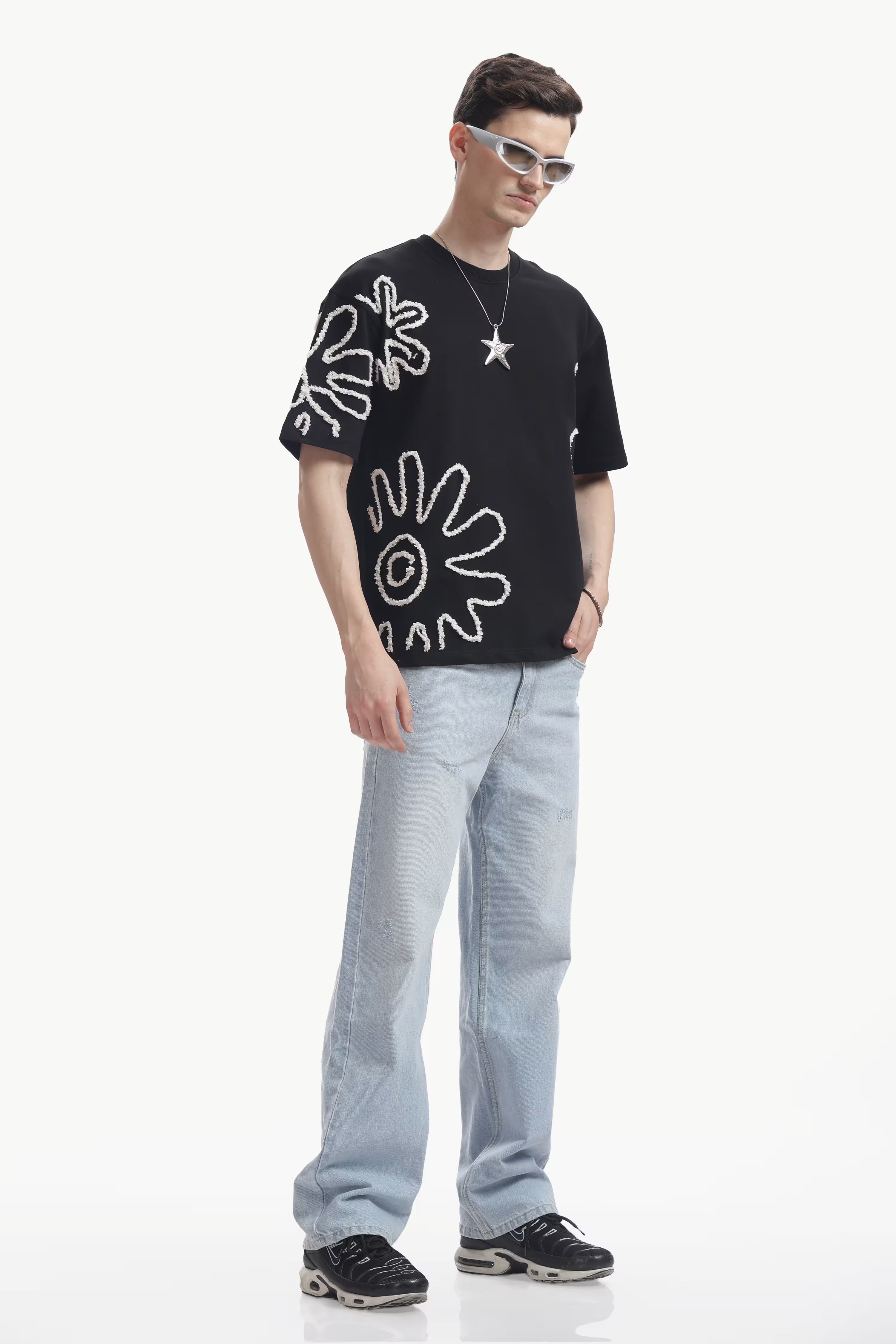 Man wearing a black t-shirt with white Embroidery Appliqués and light blue jeans on a white background