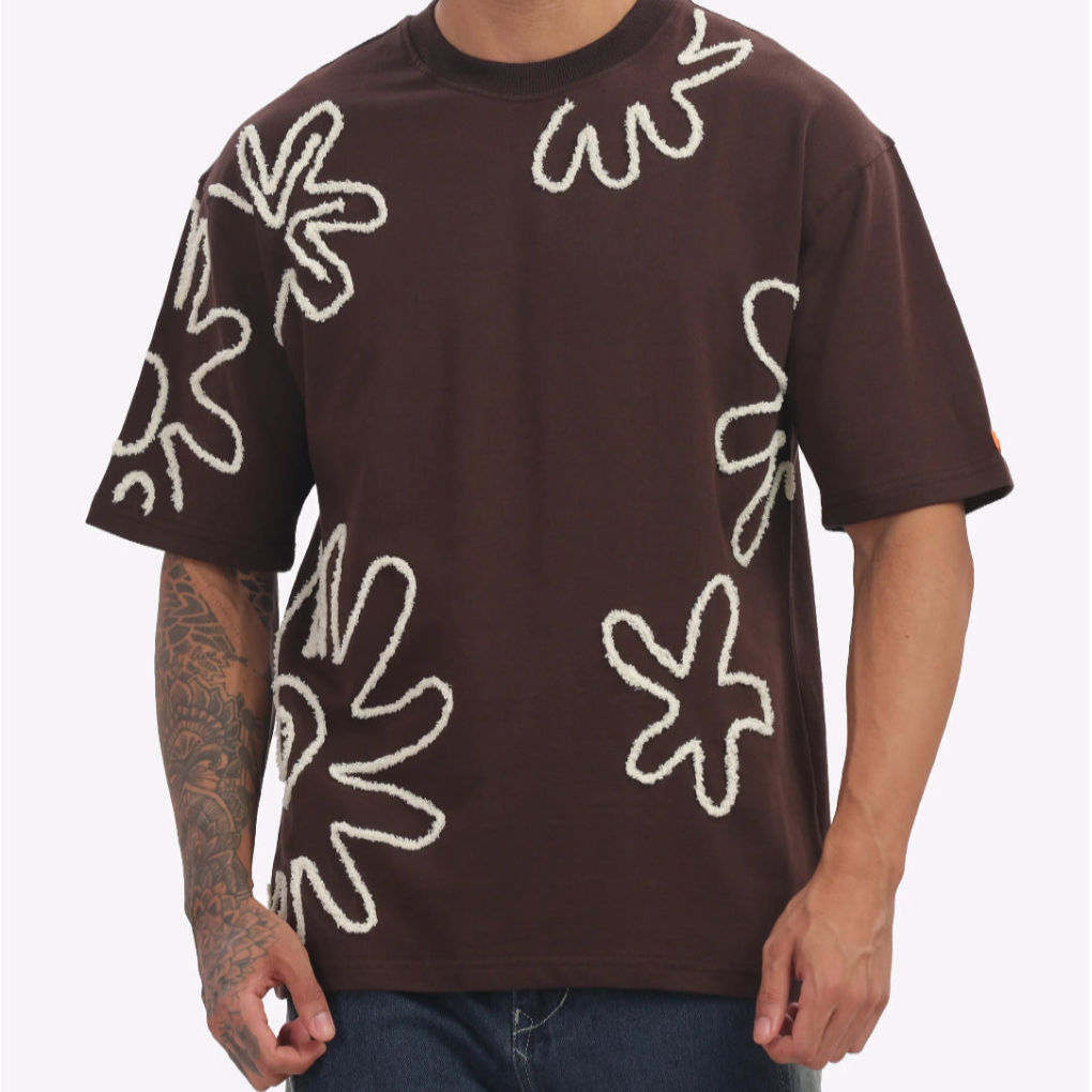 Brown t-shirt with white abstract patterns worn by a person on a plain background