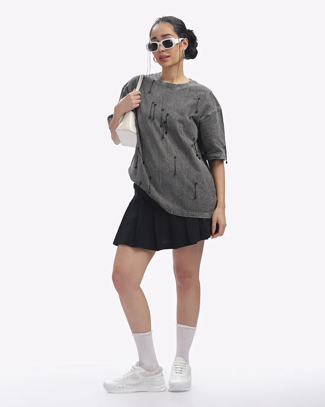 Person wearing a gray oversized shirt, black skirt, white sneakers, and sunglasses on a white background