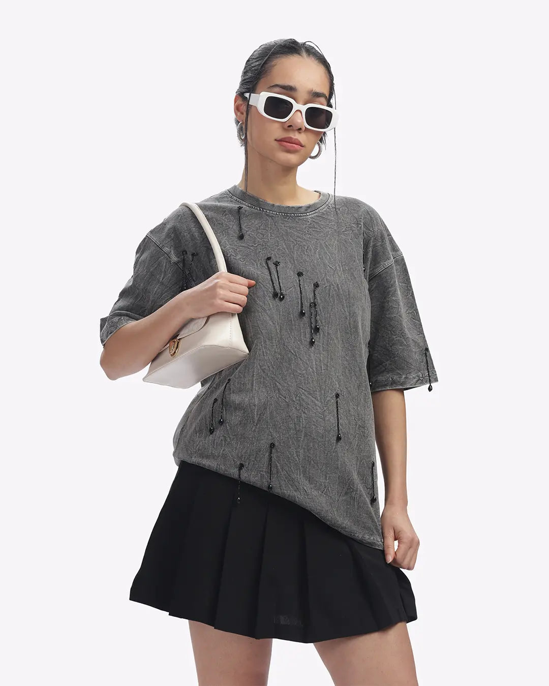 Woman wearing a gray oversized top and black skirt with sunglasses on a white background