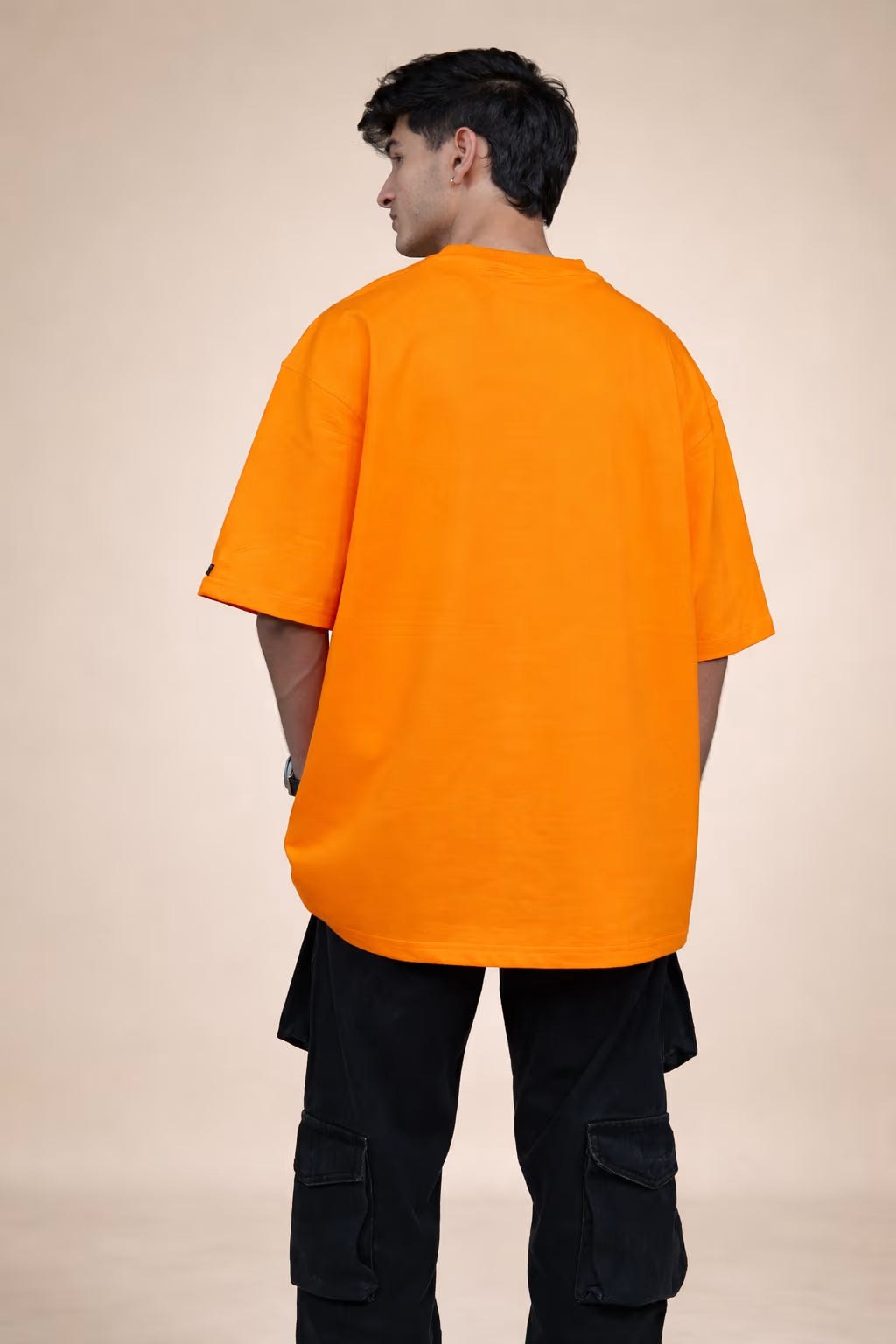 Person wearing an orange t-shirt and black pants on a beige background