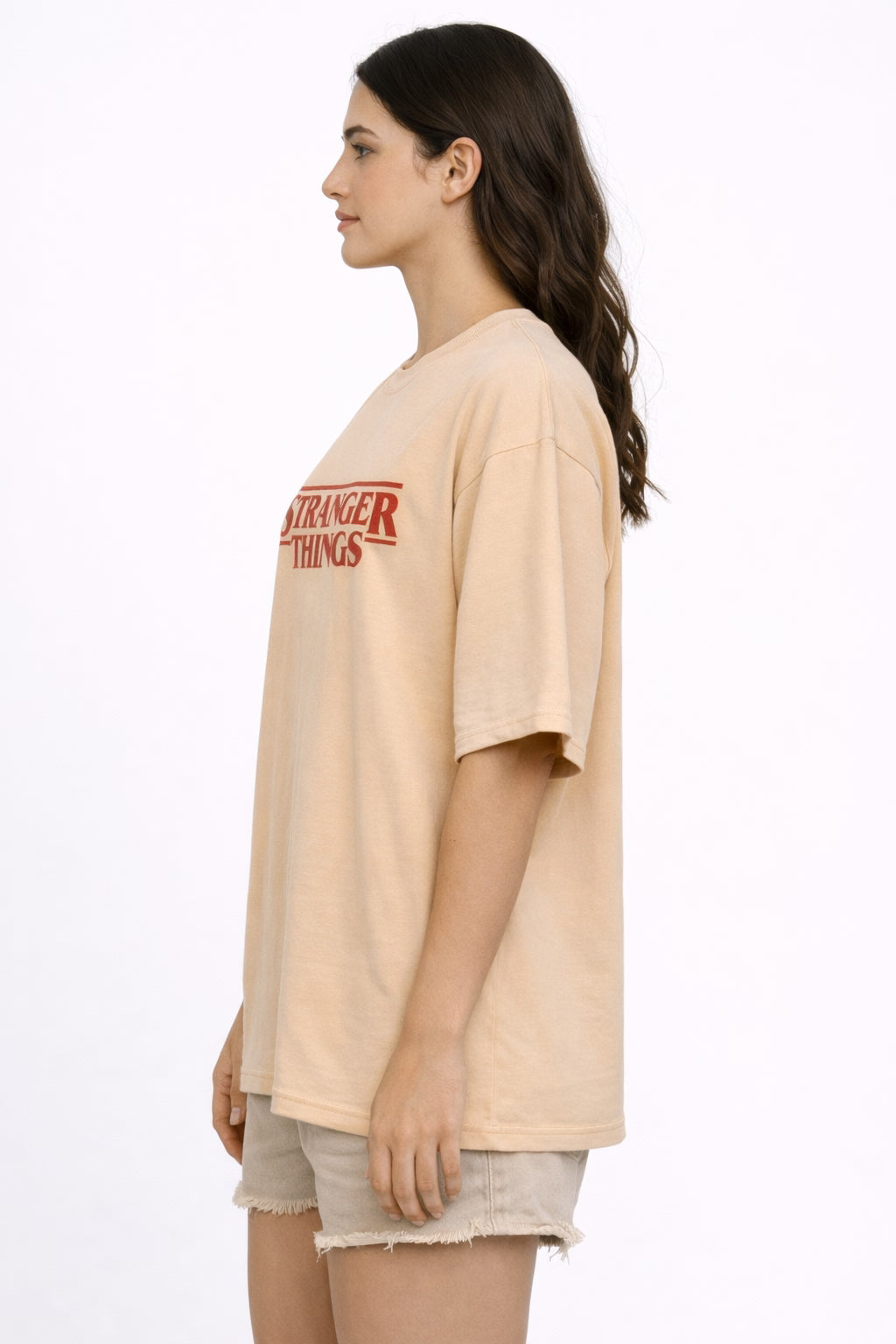 Woman wearing a beige oversized  t-shirt with 'Stranger Things' logo on a white background