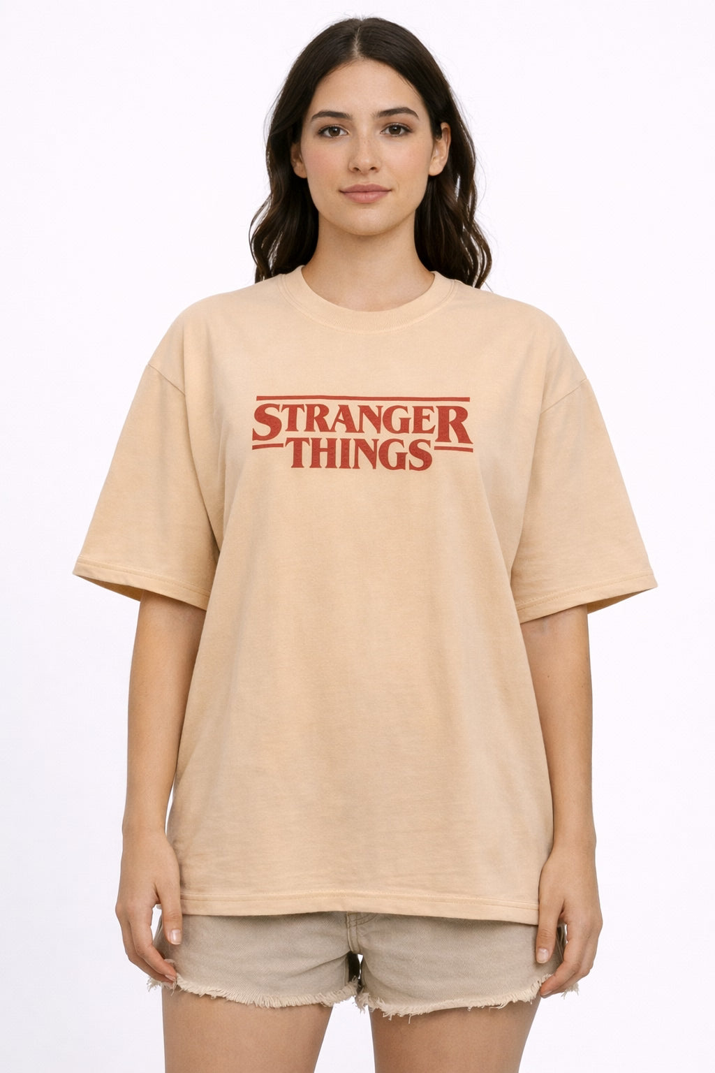 Woman wearing a beige oversized  t-shirt with 'Stranger Things' logo on a white background