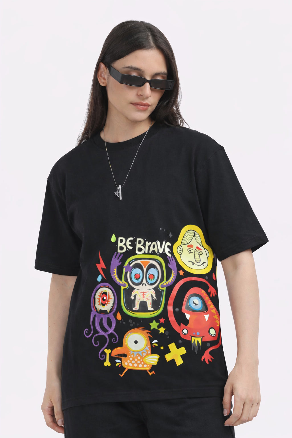 Person wearing a black t-shirt with colorful graphics BE Brave and light gray pants on a white background