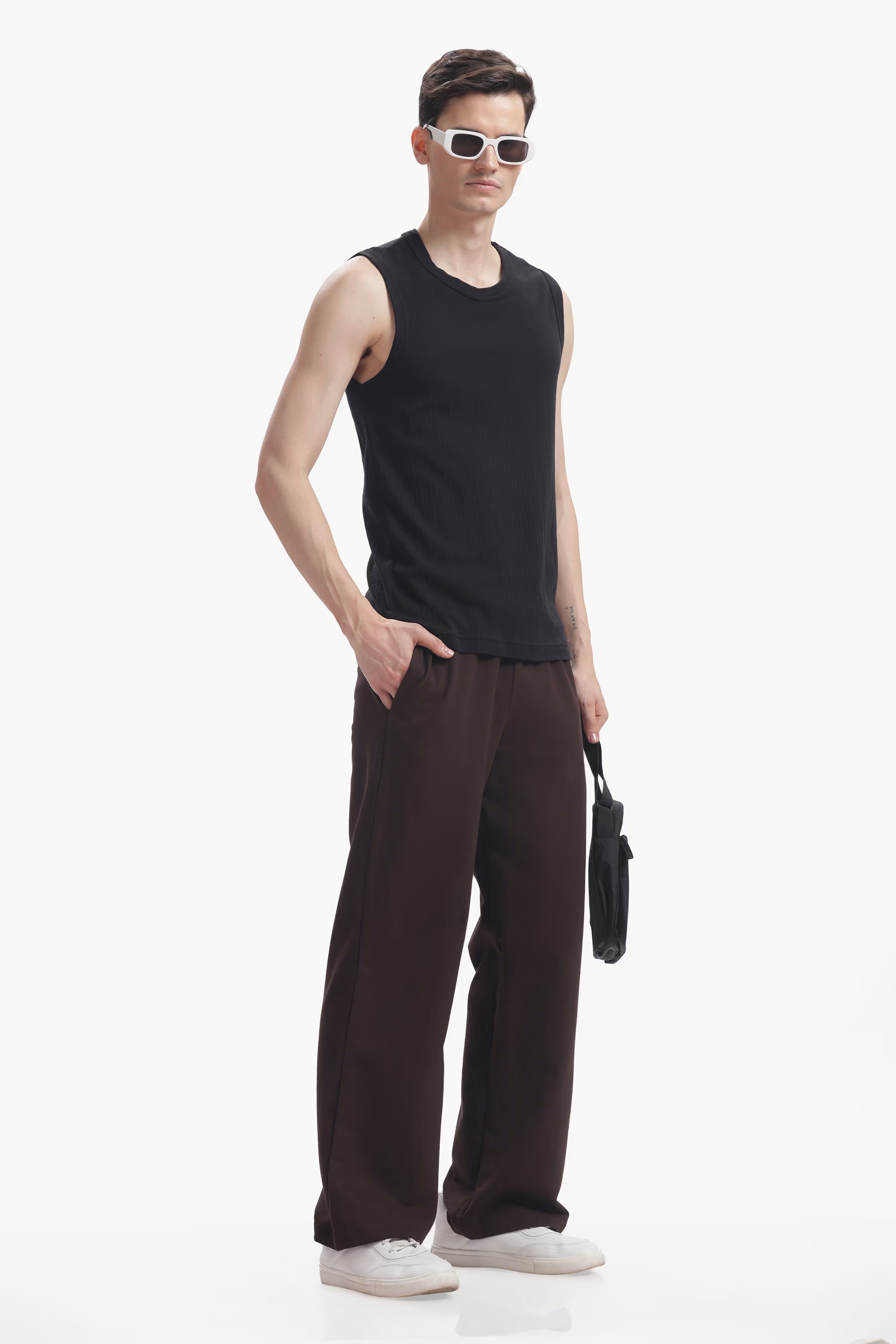 Man wearing a black sleeveless shirt and brown pants holding a black bag on a white background