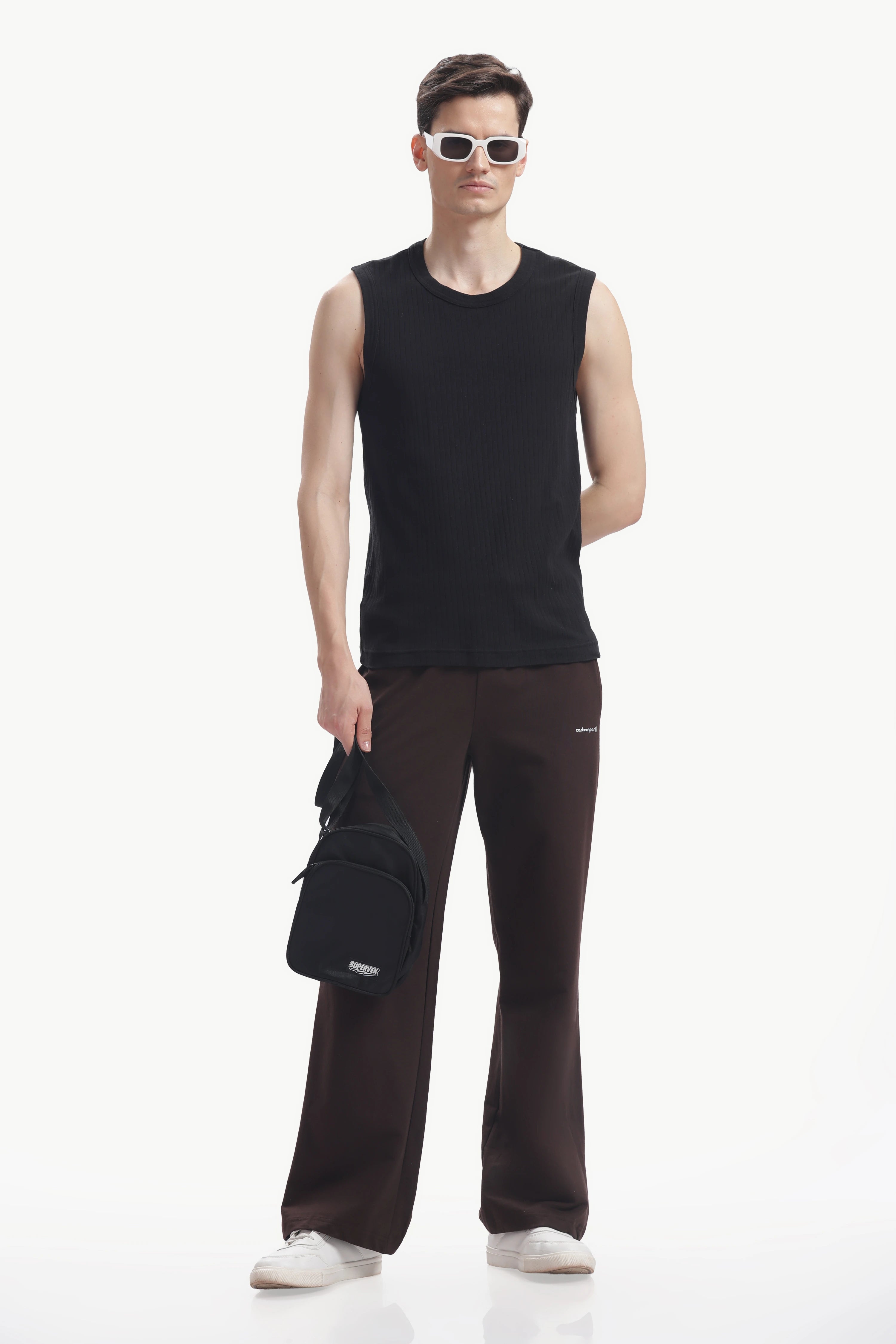 Person wearing a black sleeveless shirt and brown pants with a black bag on a white background