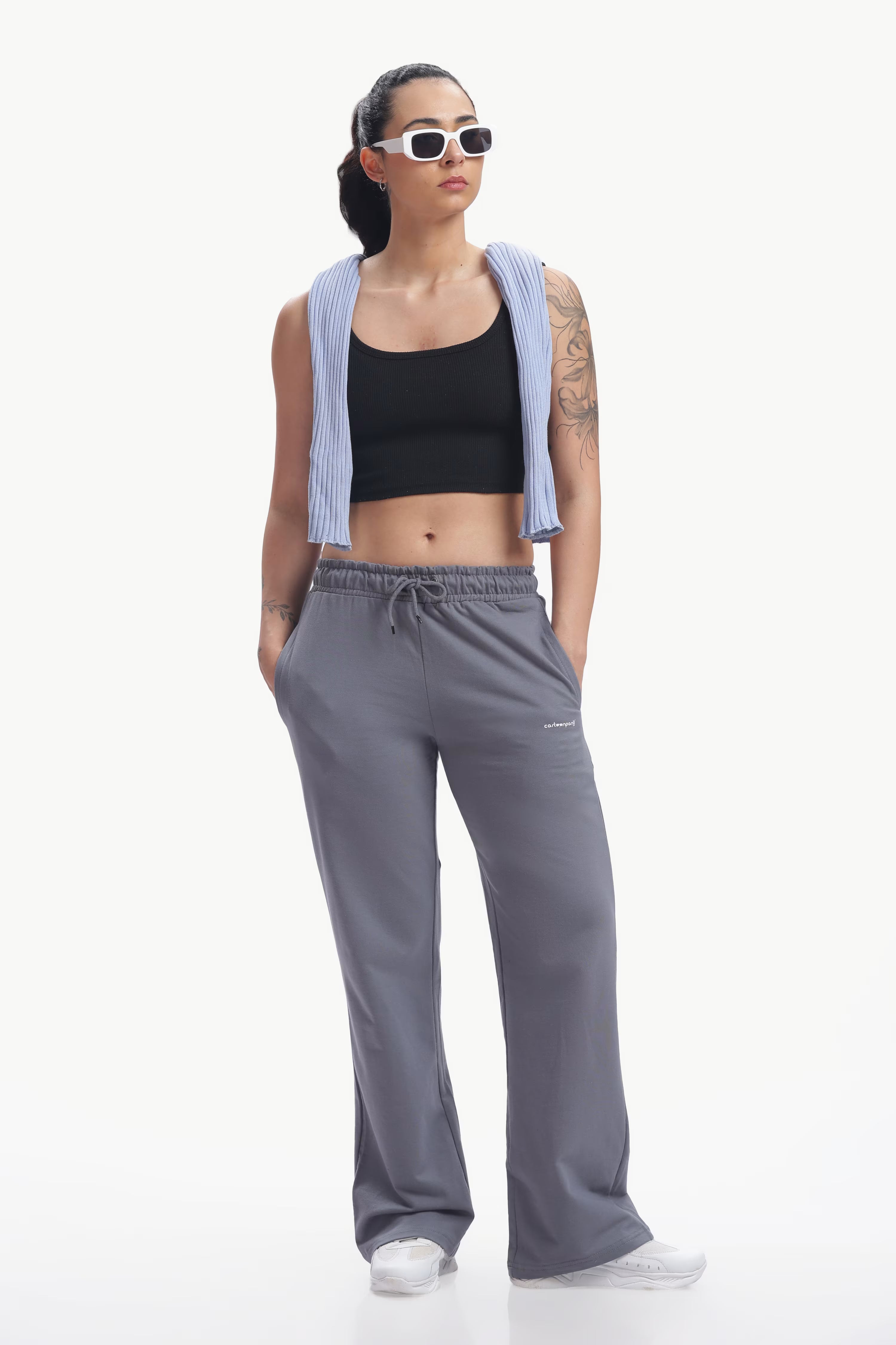 Woman wearing a black crop top, gray sweatpants, and sunglasses on a white background