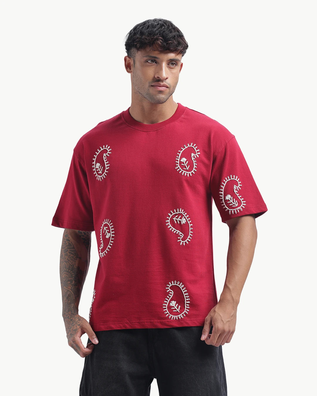 Person wearing a mahroon emboidery t-shirt with a white logo on the back, standing against a white background