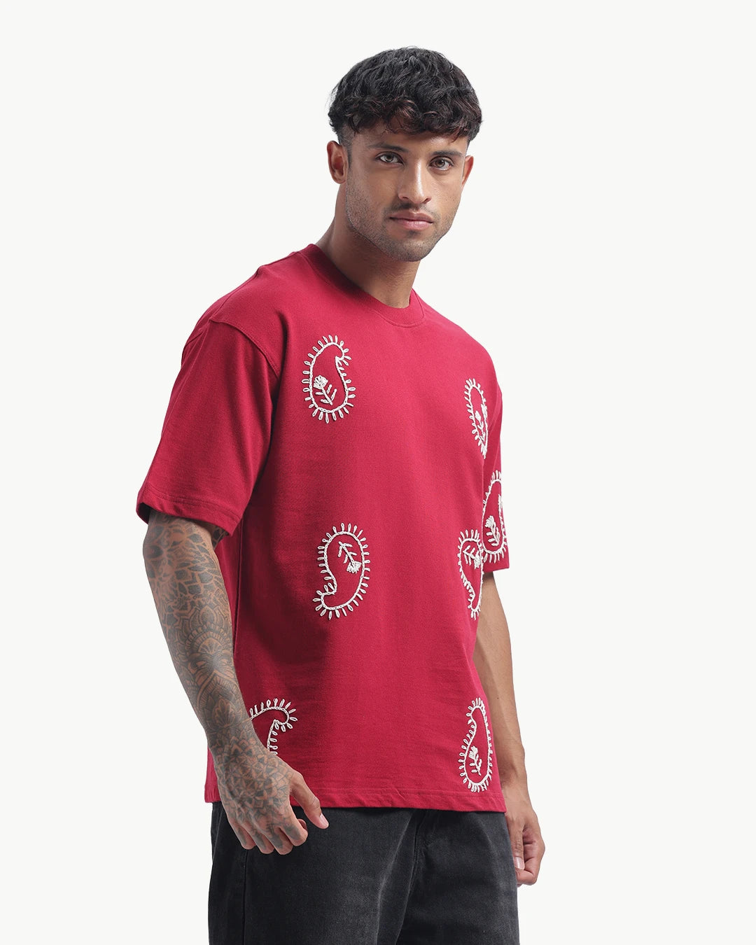 Person wearing a mahroon emboidery t-shirt with a white logo on the back, standing against a white background