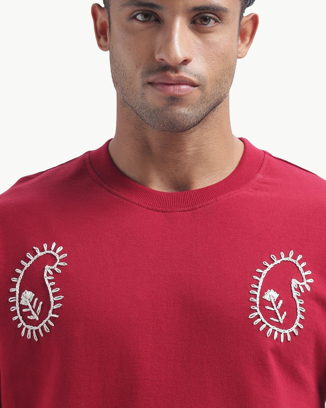 Person wearing a mahroon emboidery t-shirt with a white logo on the back, standing against a white background