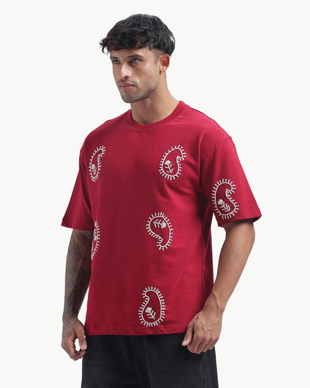 Person wearing a mahroon emboidery t-shirt with a white logo on the back, standing against a white background