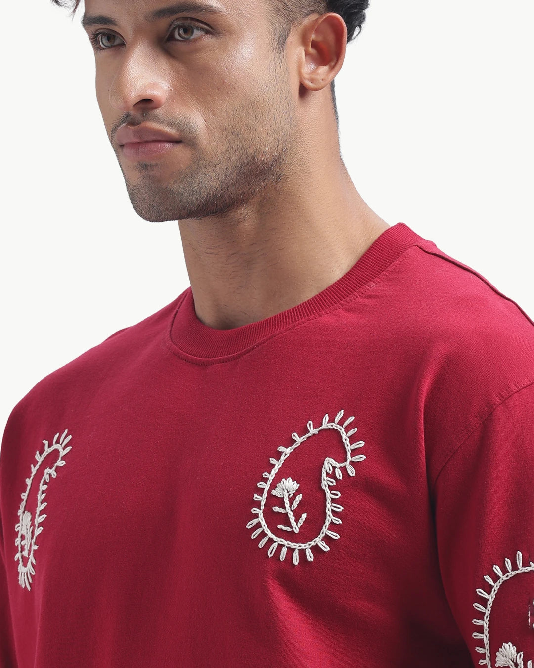 Person wearing a mahroon emboidery t-shirt with a white logo on the back, standing against a white background