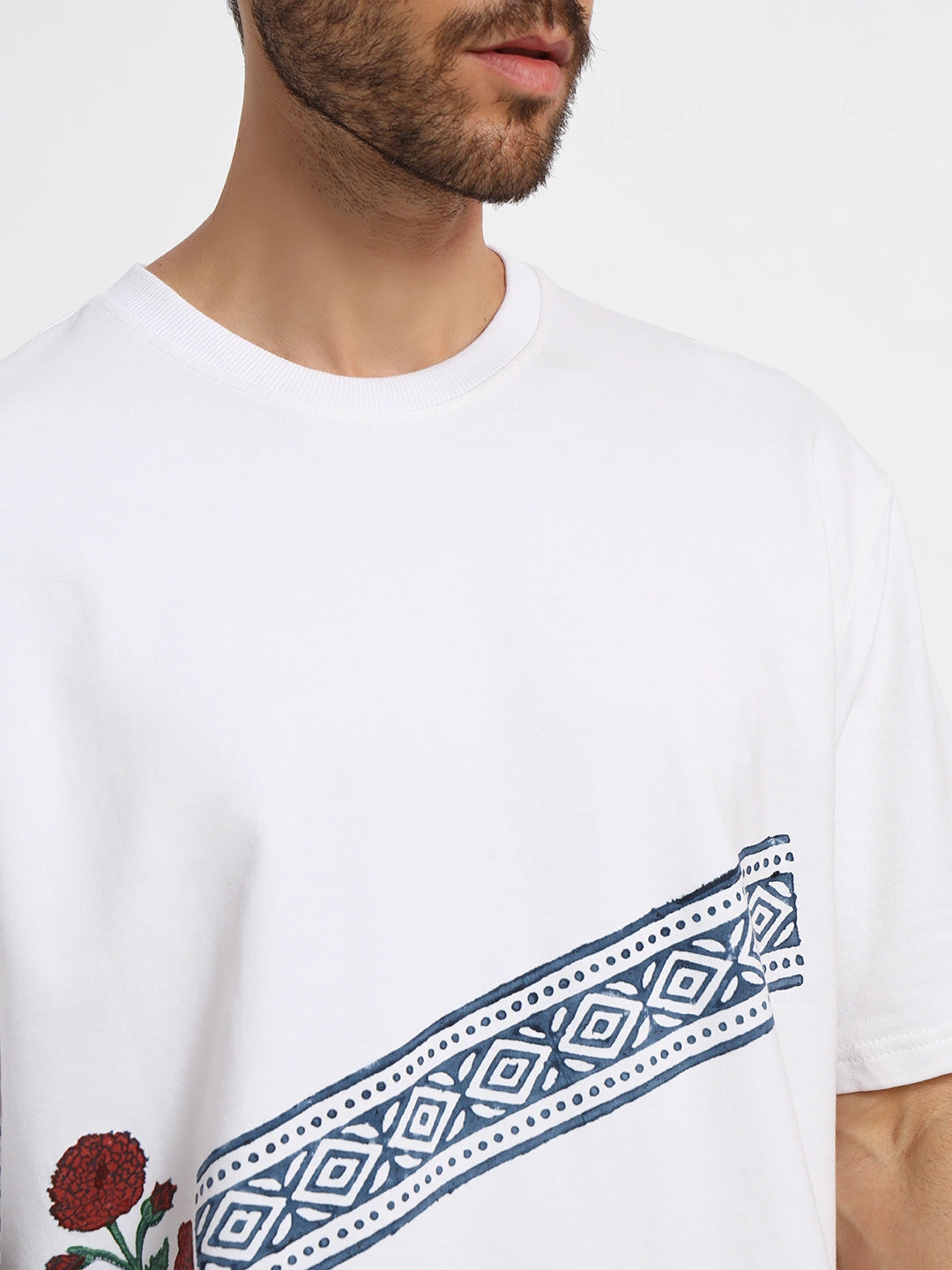 White oversized t-shirt with blue geometric design and red floral elements worn by a person.