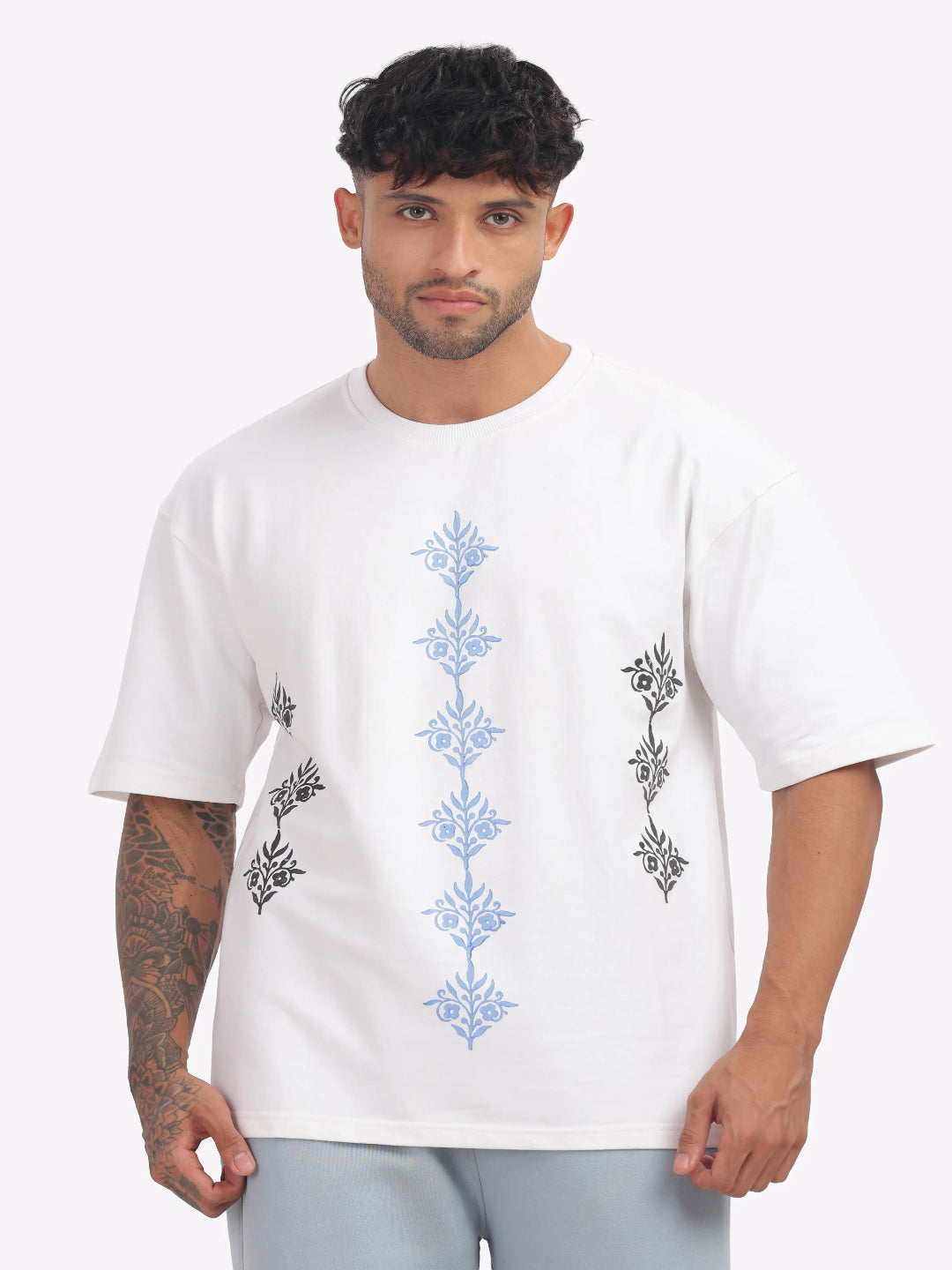 Man wearing a white t-shirt with floral embroidery on a plain background