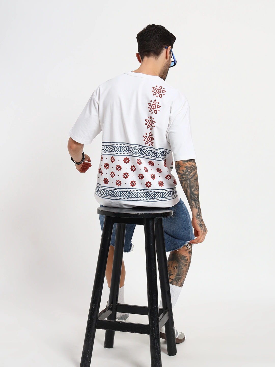 Person wearing a white t-shirt with patterns, standing on a black stool against a white background  by cartoonpanti india